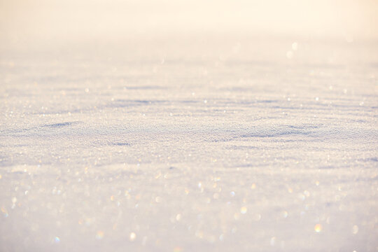 Texture of white snow sparkling in the sun. The foreground and background are blurred.
