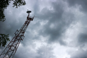 mobile phone mast with satellite antenna against stormy sky with clouds