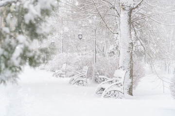 winter city park, benches covered in snow and snowfall