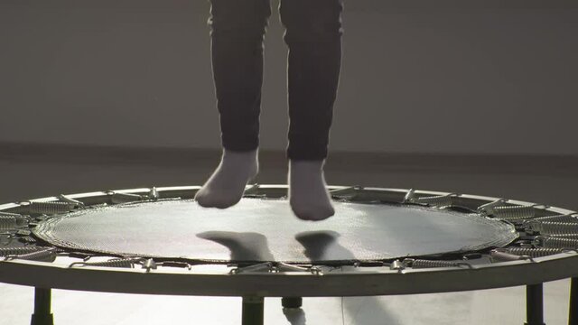child girl jumping on a trampoline indoors, kid feet close up in sunlight