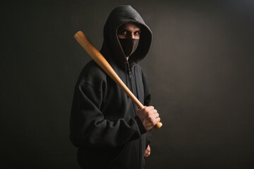 Bandit in a black sweatshirt and a medical mask. Dangerous man with a baseball bat ready to fight.