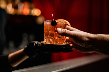 Close-up view of man's hand taking glass with cocktail from hand of woman bartender