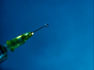 A syringe with liquid drop on blue background