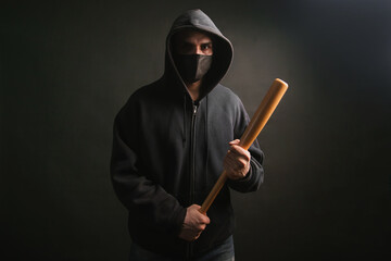 Bandit in a black sweatshirt and a medical mask. Dangerous man with a baseball bat ready to fight.