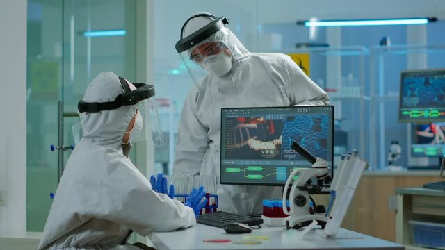 Scientist team in prorection suit arguing in front of pc looking at virus development in equipped laboratory.Team of scientists analysing vaccine evolution using high tech for researching treatment