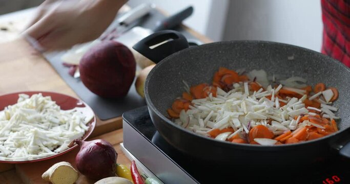 Chopped celery root added into hot pan, and mixed together with onions, red onions and carrot, preparing vegetable soup