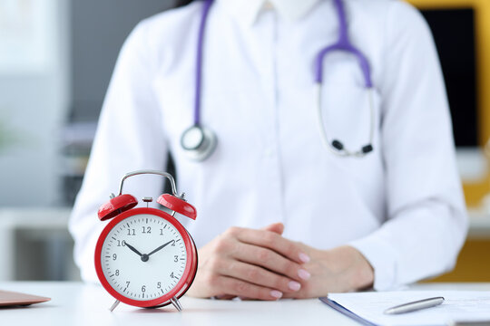 Doctor therapist sitting in office in front of red alarm clock closeup