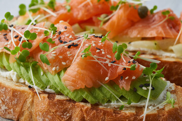 Two open sandwich, toast with salmon, cream cheese, avocado, cucumber slices on white concrete table. Morning healthy breakfast with fish and cup of drink, side view, close up, macro