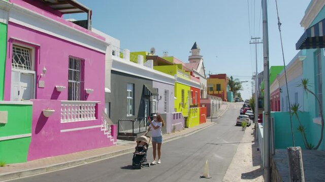 Woman walking with son and baby stroller in the streets of colorful buildings neighbourhood Bo-Kaap Cape Town South Africa.