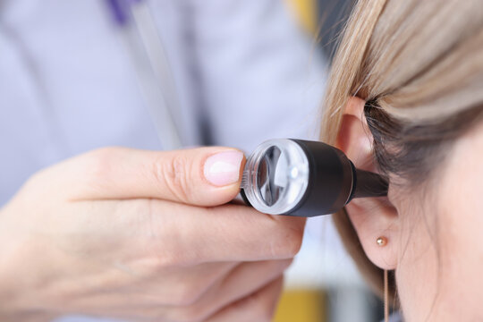 Otorhinolaryngologist looking at patients ear using an otoscope closeup