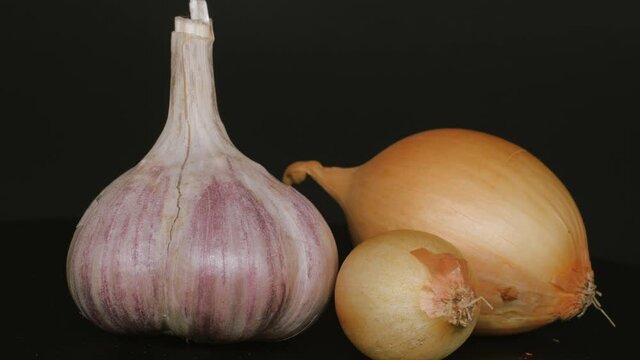 Head of garlic and two onions on a black background.
