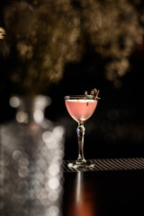 beautiful crystal glass with cocktail decorated with blooming twig stands on the bar.