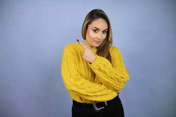 Fototapeta premium Young beautiful blonde woman with long hair wearing a yellow sweater surprised pointing with hand and finger to the side