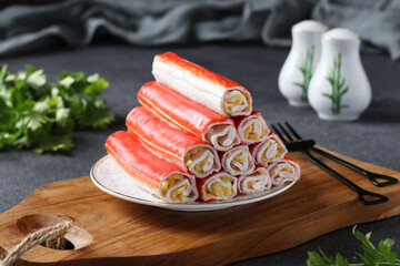 Crab sticks stuffed with rice, egg and green onions on a wooden board on a gray background. Closeup © Anzhela