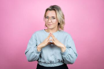 Young caucasian woman wearing sweatshirt over pink background with Hands together and fingers crossed smiling relaxed and cheerful. Success and optimistic