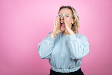 Young caucasian woman wearing sweatshirt over pink background shouting and screaming loud to side with hands on mouth