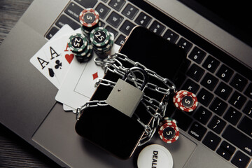 Law and rules for online gambling concept, smartphone with padlock and playng cards on laptop keyboard.