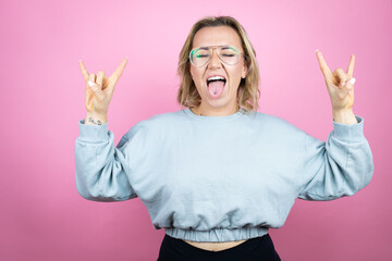 Young caucasian woman wearing sweatshirt over pink background shouting with crazy expression doing...