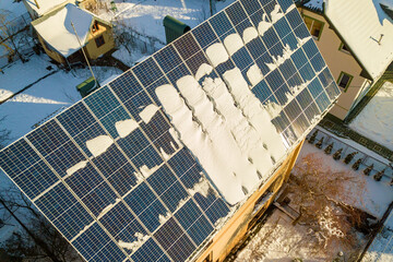 Close up surface of a house roof covered with solar panels in winter with snow on top. Energy efficiency and maintenance concept.