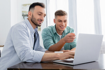 Fototapeta na wymiar homosexual man pointing with finger and looking at laptop near happy husband
