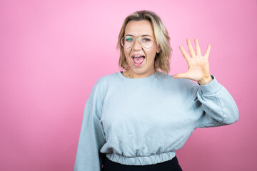 Young caucasian woman wearing sweatshirt over pink background showing and pointing up with fingers number five while smiling confident and happy