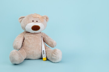 Stuffed Bear animal holding a thermometer as a symbol of children healtcare concept isolated on blue background.