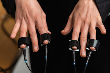 Close-up view of a suspect's hand connected to a lie detector / polygraph test machine while a male...