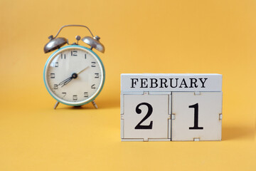 Calendar for February 21: cubes with the number 21 and the name of the month, alarm clock on a yellow background
