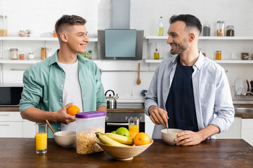 happy same sex couple looking at each other near tasty breakfast on table
