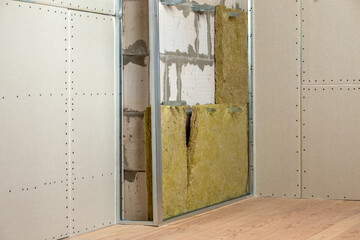 Wall of a room under renovation with mineral rock wool insulation and metal frame prepared for drywall plates.