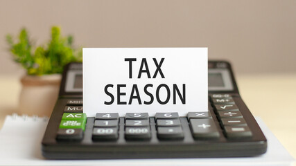 Paper card with text TAX SEASON. Calculator, flowers and brown background