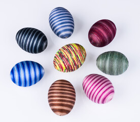 Group of colored Easter eggs with striped pattern on a white background. Collection of hollow shells hand-decorated by pasted sewing cotton yarn. Set of various streaked holiday decorations. Top view.