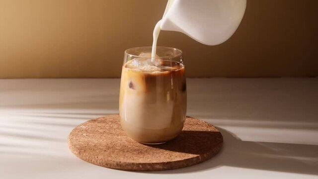 Milk cream is pouring into a iced coffee. Cold brewing coffee drink glass with ice and milk.