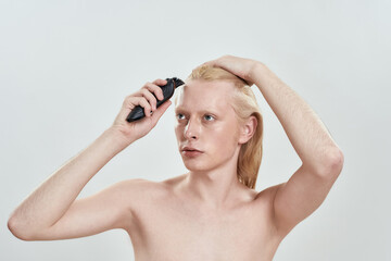 Naklejka premium Young caucasian blond man using hair trimmer