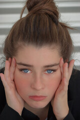 Fototapeta premium Close up outdoor portrait of the face of a young woman with long brown hair while she holds her face. Fashion Model 2021.