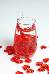 Valentine's Day. Small red glass hearts in a glass of water. A splash of liquid.