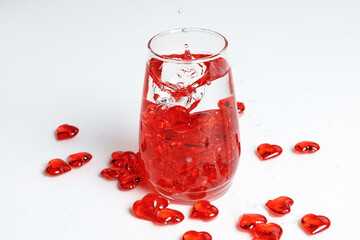 Valentine's Day. Small red glass hearts in a glass of water. A splash of liquid.
