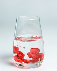 Valentine's Day. Small red glass hearts in a glass of water. A splash of liquid.