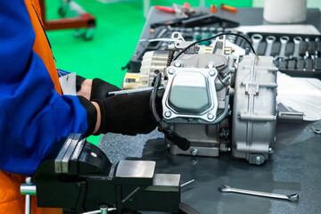 Fototapeta premium Hands of a car foreman during work. He's fixing some car part. Man in a uniform works with auto parts. Concept is a career as automotive locksmith. Work in a car workshop. Manufacturing of auto parts