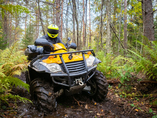 Fototapeta na wymiar ATV racing in the woods. Extreme ATV racing off-road. Biker's journey in woods. Biker on a yellow ATV. Portrait of a biker in mud. Motocross in the green taiga. Participation in motocross