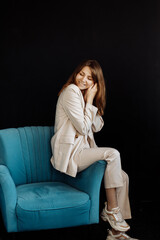 Obraz premium Happy cheerful business woman sitting in the studio in a chair. Posing for the camera with closed eyes. A young girl with a wide smile, she feels free from the hardships of life.