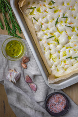 The process of making focaccia of natural sourdough with rosemary and garlic. Whole grain dough before baking on a wooden background. Artisan