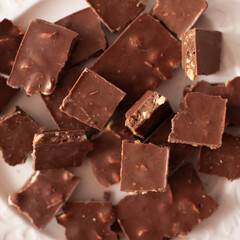 Chopped chocolate bars with nuts on white plate close up. Top view.