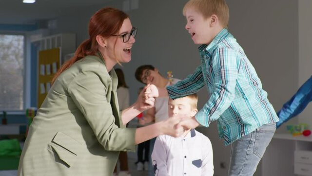 active childhood, smiling young female teacher holds the hands of a boy with down syndrome jumping on a trampoline in slow motion