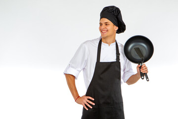 Young cook is holding a frying pan. Chef guy on a white background. Man in a cook's uniform smiles. Portrait of a restaurant chef. culinary student portrait. Young guy is learning to be a cook.