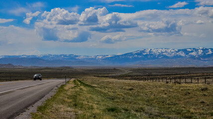 The landscape is in the wild. A road going into the distance, white clouds on the horizon.