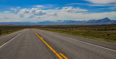 The landscape is in the wild. A road going into the distance, white clouds on the horizon.