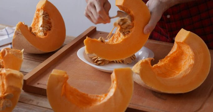 Sweet pumpkin prepared for roasting, removing seeds using spoon, close-up on hands, unrecognizable person