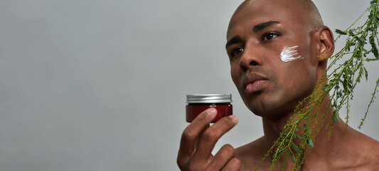 Mixed-race man raising a skin care cream near plant