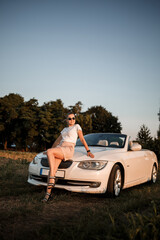 A beautiful young woman of European appearance on the face of sunglasses, she stands near her white convertible. Successful woman businesswoman and her white car.